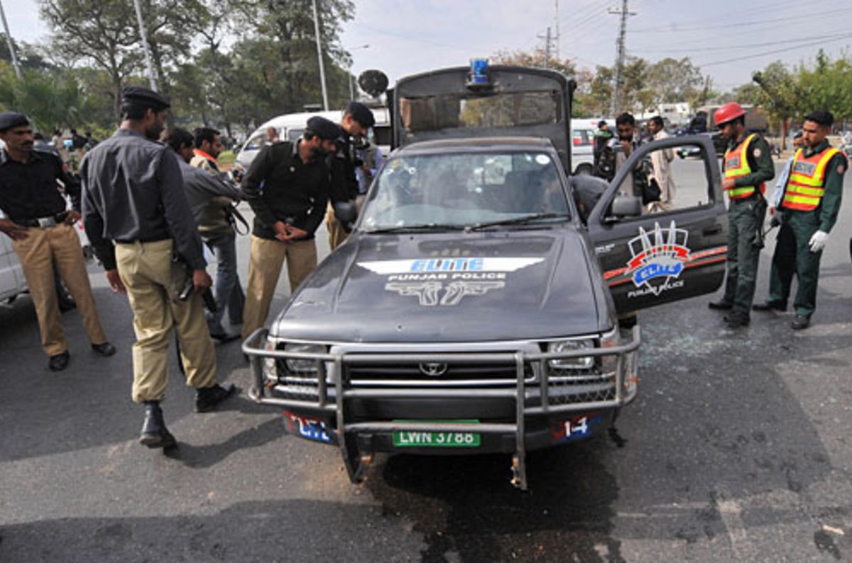 Security guards inspect a damaged vehicle after the firing in Lahore ...