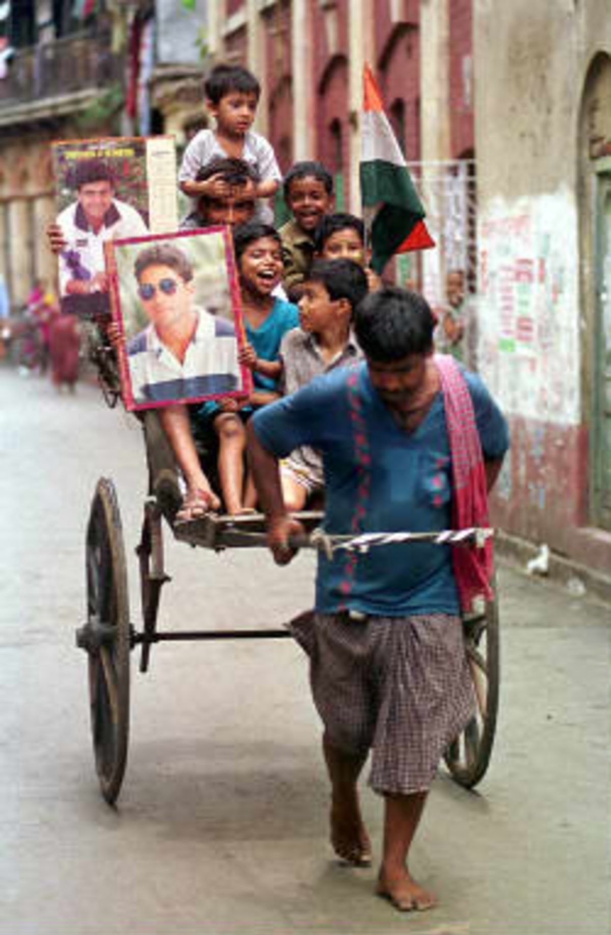 A rickshaw puller tows a load of children brandishing the Indian flag and pictures of their cricketing idols in Calcutta 27 May 1999, to celebrate India's roundly defeating Sri Lanka in the preliminary round of the cricket World Cup in England