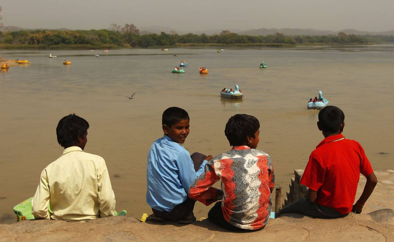 Four boys watch visitors cruise in boats on Sukhna Lake in Chandigarh, March 26, 2010