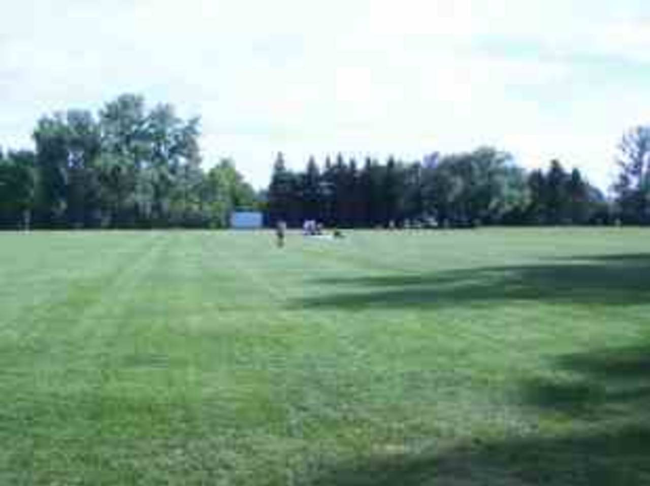 Riley Park, Calgary, 2002. A view from the north of one of the cricket fields in Riley Park, Calgary, with the matting being removed following the conclusion of an evening match. In the background to the right is the second field. The beautiful sunny mid-summer evening sees the field already used by soccer players for a late practice.