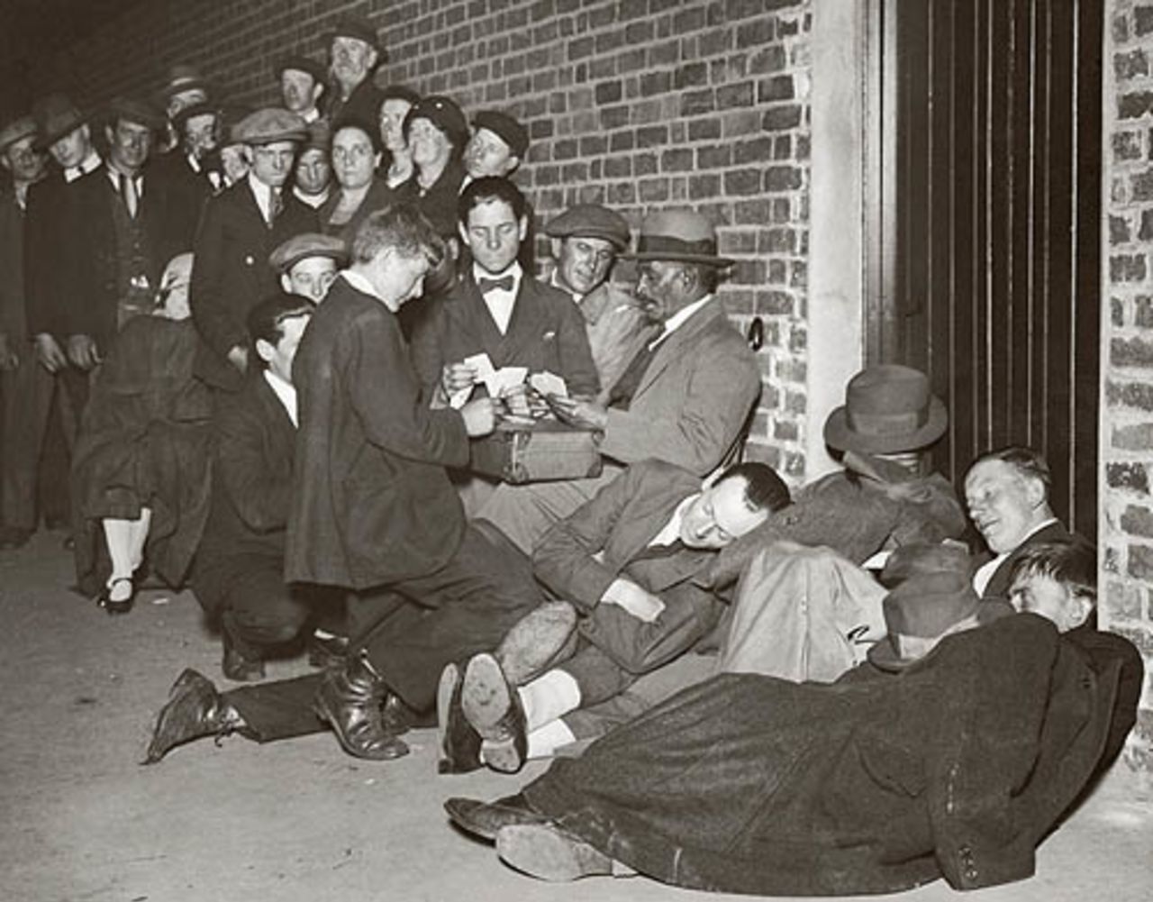Cricket fans pass time with a game of cards in an all-night queue outside Lord's, circa 1930