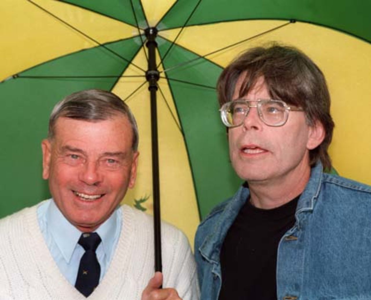 Umpire Dickie Bird (left) and novelist Stephen King under an umbrella as rain stops play during King's visit to Trent Bridge, 23 August 1998