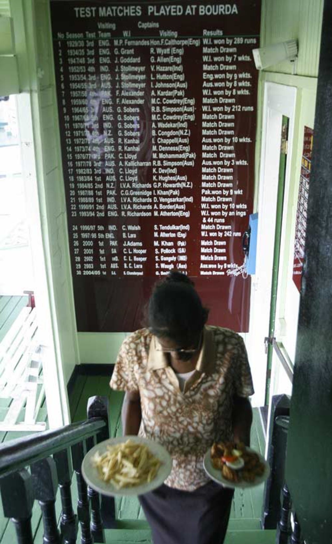 A waitress passes a board that displays details of matches played at the Bourda Oval in Georgetown, Guyana, 5 April 2007