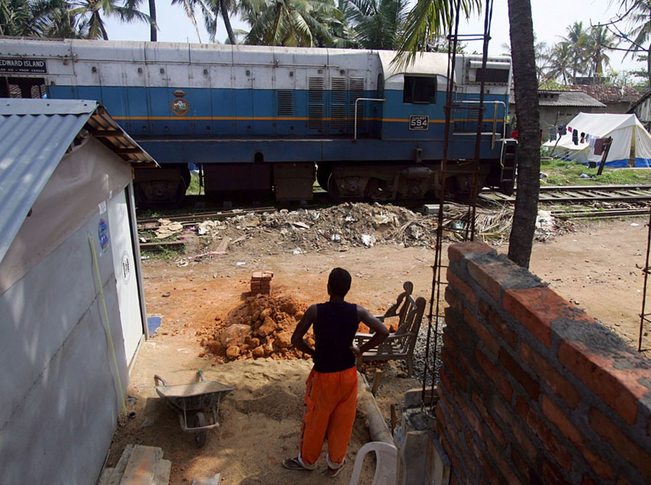 The "Queen of The Sea" train rolls by as a man looks out next to his USAID temporary shelter along the railroad tracks, Galle, June 25, 2005