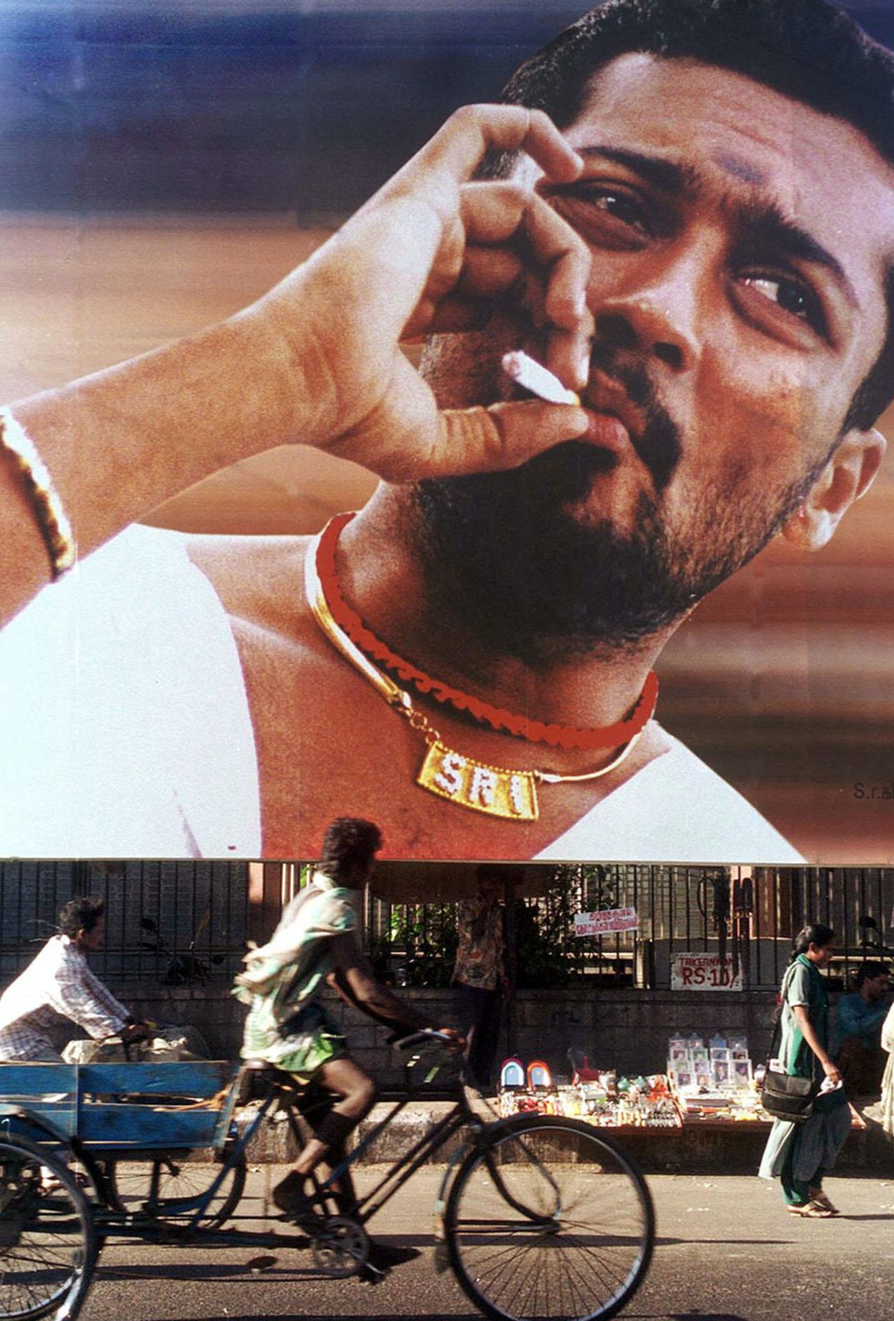 A rickshaw passes by a film poster showing Tamil actor Surya smoking a cigarette, Chennai, March 15, 2002