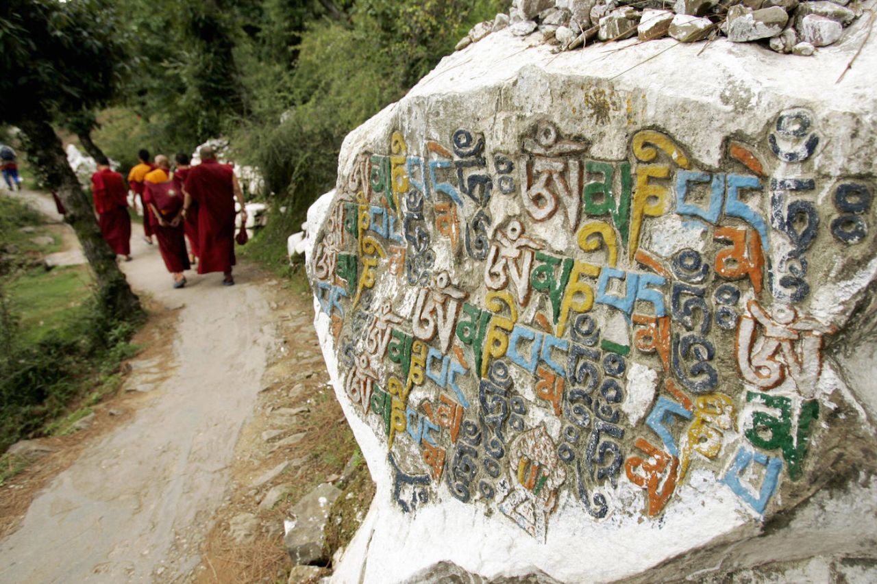 Tibetan Buddhist monks walk on a cloudy mountain path past Buddhist scriptures engraved on a rock in Dharamsala, 05 July 2005