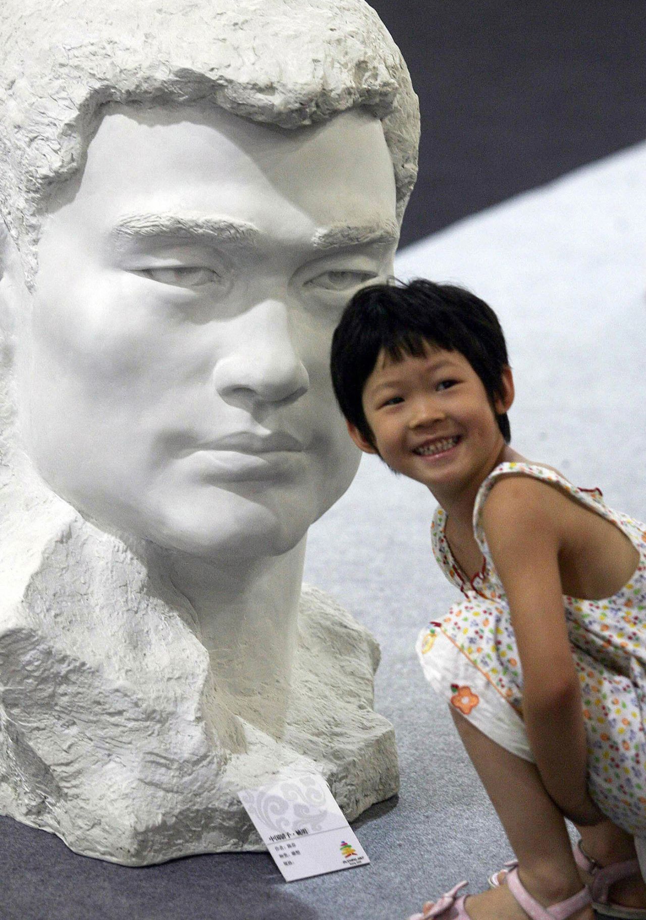 A child poses next to the bust of basketball superstar Yao Ming on display at the Olympic Games fine arts exhibition in Beijing, August 20, 2008