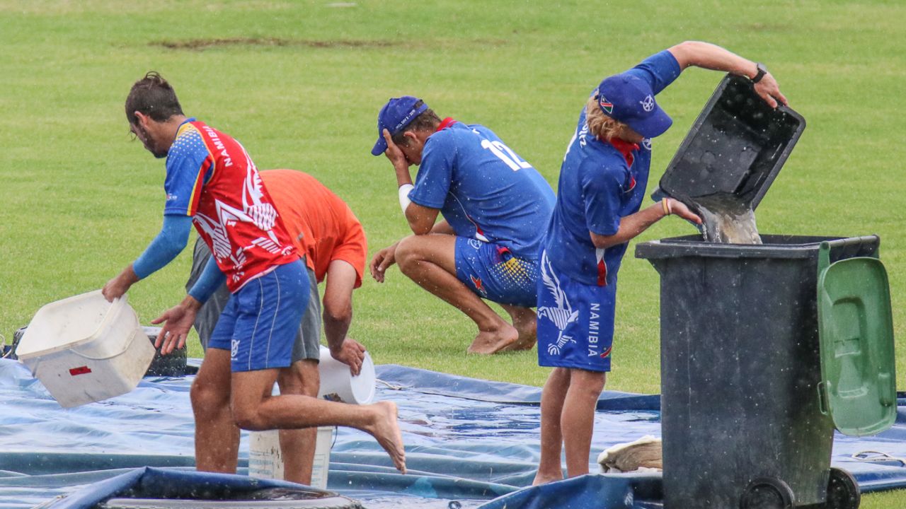 Bernard Scholtz empties water off the covers as JJ Smit crouches in frustration over the falling rain, Namibia v Kenya, ICC World Cricket League Division Two, Windhoek, February 10, 2018