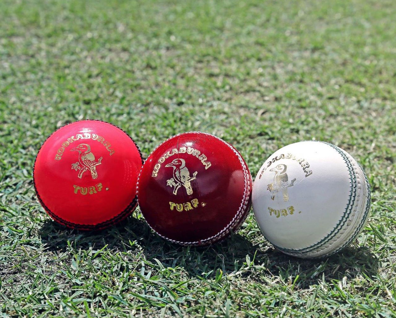 Three Kookaburra balls, pink, red and white on the grass