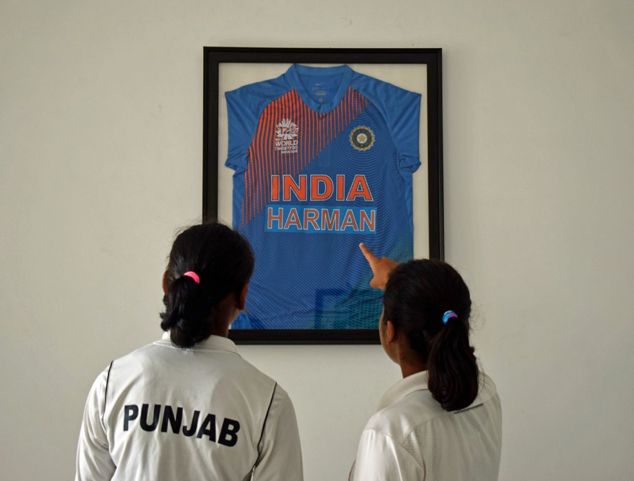 Avreet Kaur (left) and Ramanpreet Kaur, who study at Gian Jyoti School in Moga Punjab, look at a framed jersey of Harmanpreet's in the school's found Kamaldheesh Sodhi's office, July 23, 2018