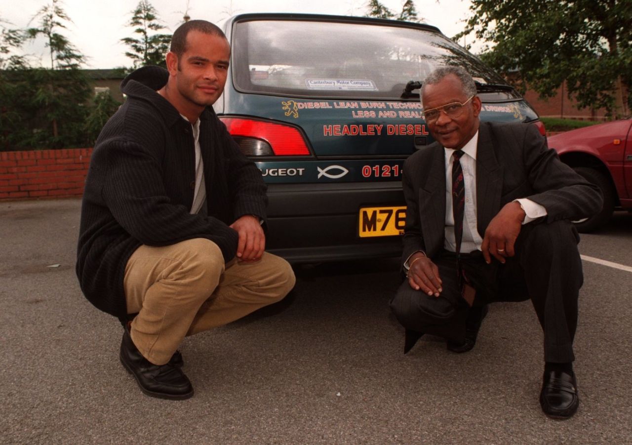 Dean and Ron Headley pose in front of an advertisement for their firm, England, July 2, 1997