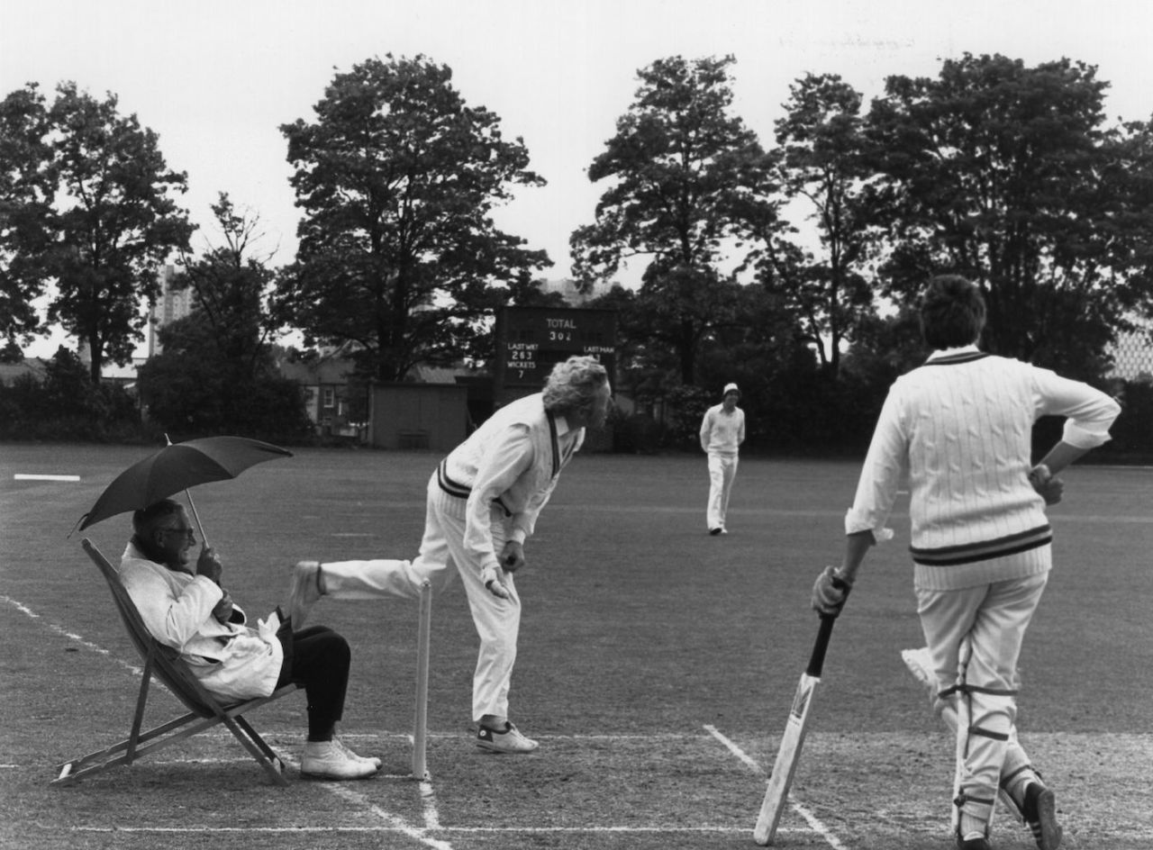 Umpire Percy Lister shelters under an umbrella during a cricket marathon at Edmonton, London, June 10, 1980
