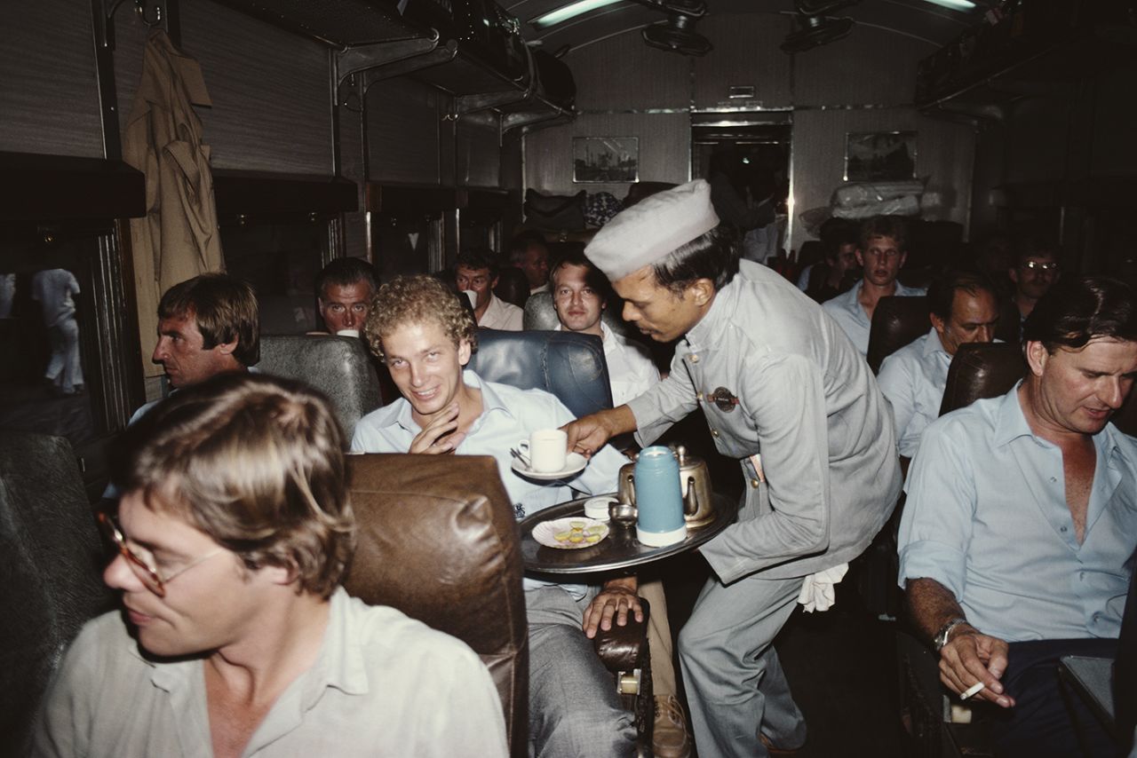 A waiter serves David Gower tea on a train from Bombay to Poona. Team-mate John Lever sits next to Gower and journalist Scyld Berry in front, November 1, 1981