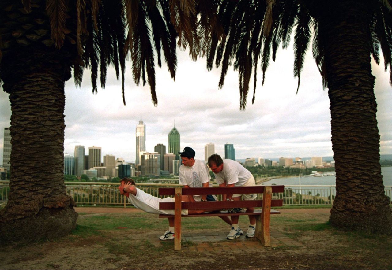 Physio Dave Roberts and Mike Gatting help Mike Atherton work out on a bench at Kings Park in Perth, October 23, 1994