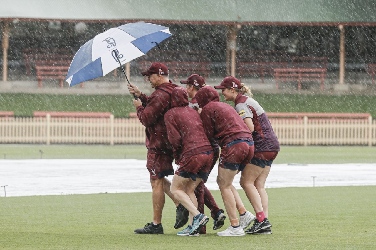 Queensland Coach Scott Prestwidge shelters players Ellie Johnston, Ruth Johnston, Holly Ferling and Georgia Redmayne under his umbrella as they inspect a rain soaked ground before the match, New South Wales and Queensland, WNCL, North Sydney Oval, on March 21, 2021 