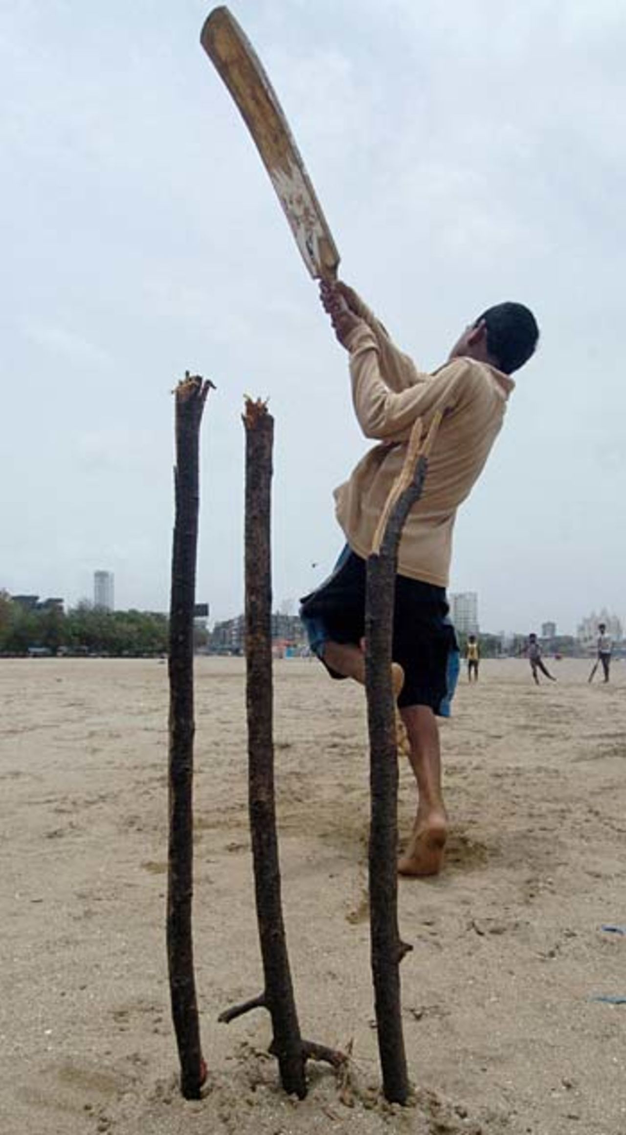 An Indian boy plays cricket using broken branches for stumps at Chowpatty Beach in Mumbai, July 4, 2005