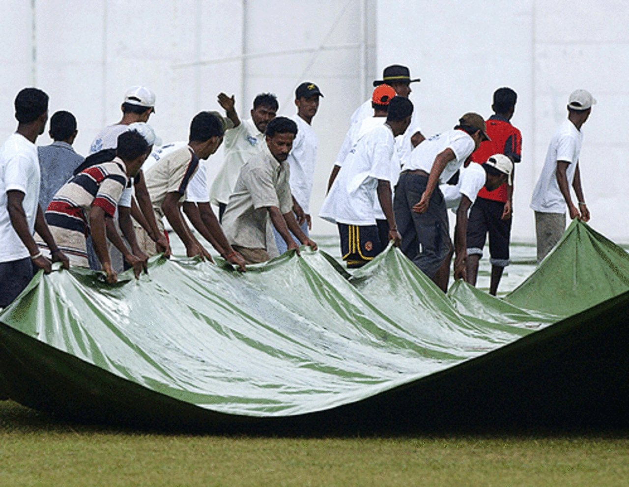 Sri Lankan ground staff pull over the covers to protect the pitch from a sudden downpour of rain prior to the start of the third day of the second and final Test match, Sri Lanka v West Indies, Kandy, July 24 2005