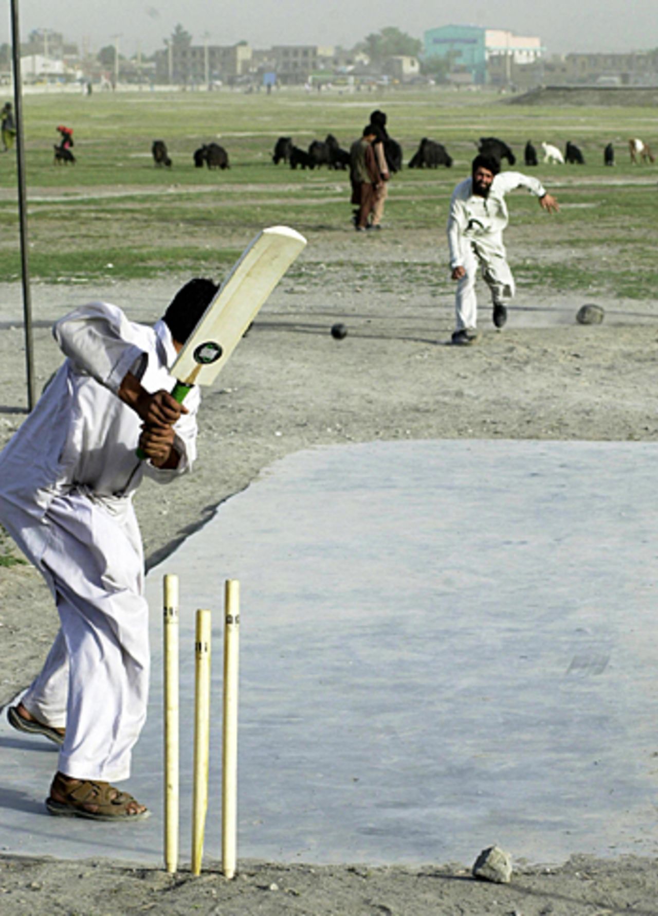 Afghan men wearing white shalwar kameez play cricket on a newly-laid pitch outside Kabul Stadium, Afghanistan, December 15, 2005