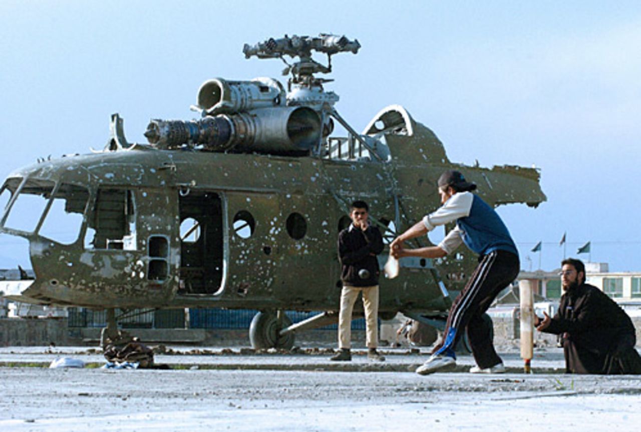 A group of Afghans play cricket in front of a destroyed helicopter, Kabul, March 17, 2005