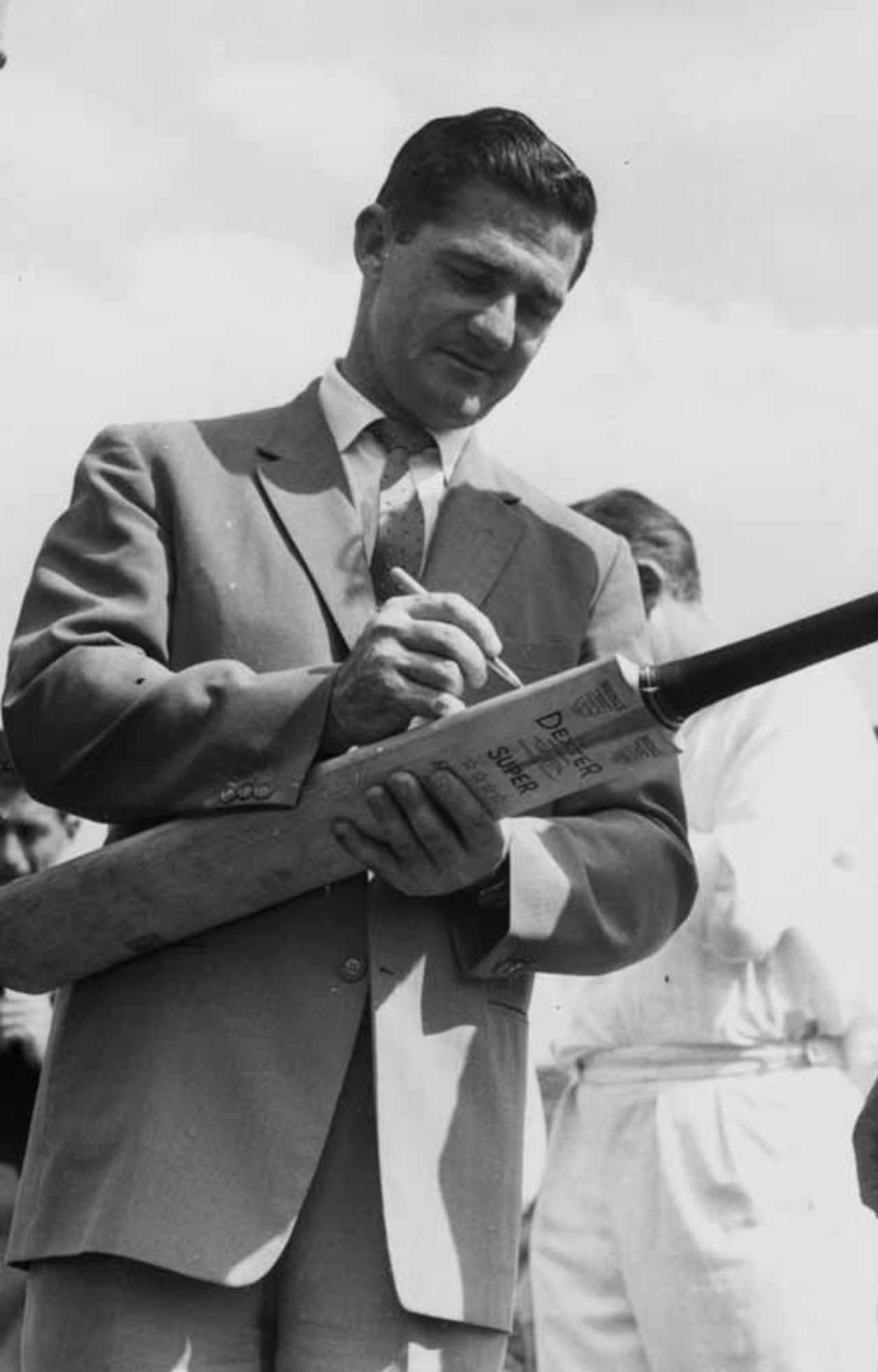 Neil Harvey autographs a cricket bat during a visit to the Governor General of Australia, at his home in Penhurst