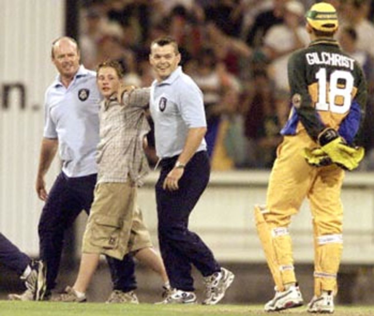 Policemen arresting a ground invader chat to Australian wicketkeeper Adam Gilchrist (R) in their match against the West Indies at the MCG in Melbourne, 11 January 2000. Australia scored 267-6 off their 50 overs and then restricted the West Indies to 193-7 from their 50 overs to go one up in the tri-nations series which also includes Zimbabwe.