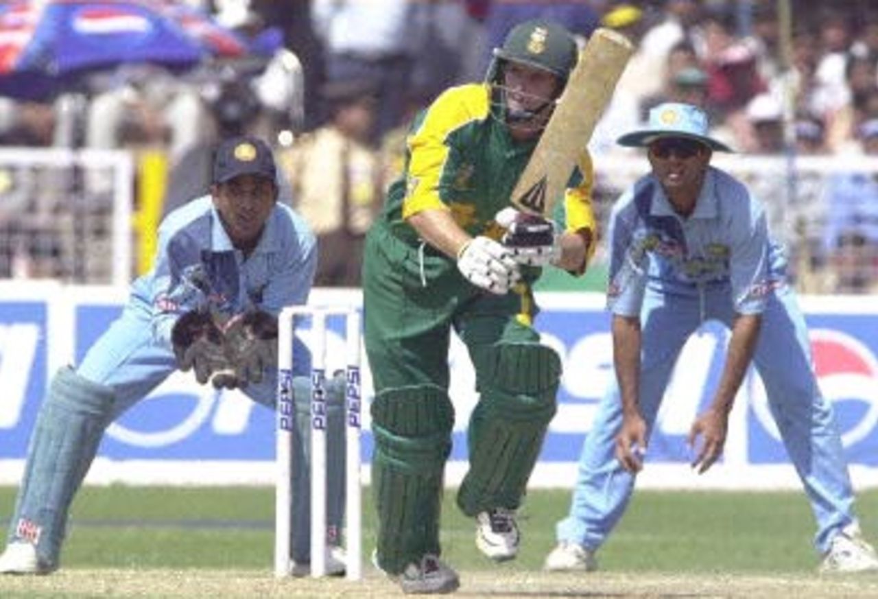 South African batsman Gary Kirsten (C) slams a ball to the boundary on his way to scoring 93 runs, the highest in the match, as Indian wicket keeper Sameer Dighe (L) and Rahul Dravid (R) look on during the third one-day international cricket match between South Africa and India played at Faridabad 15 March 2000. South Africa went on to beat India by two wickets as the five match series stands at 2-1 in favour of India.