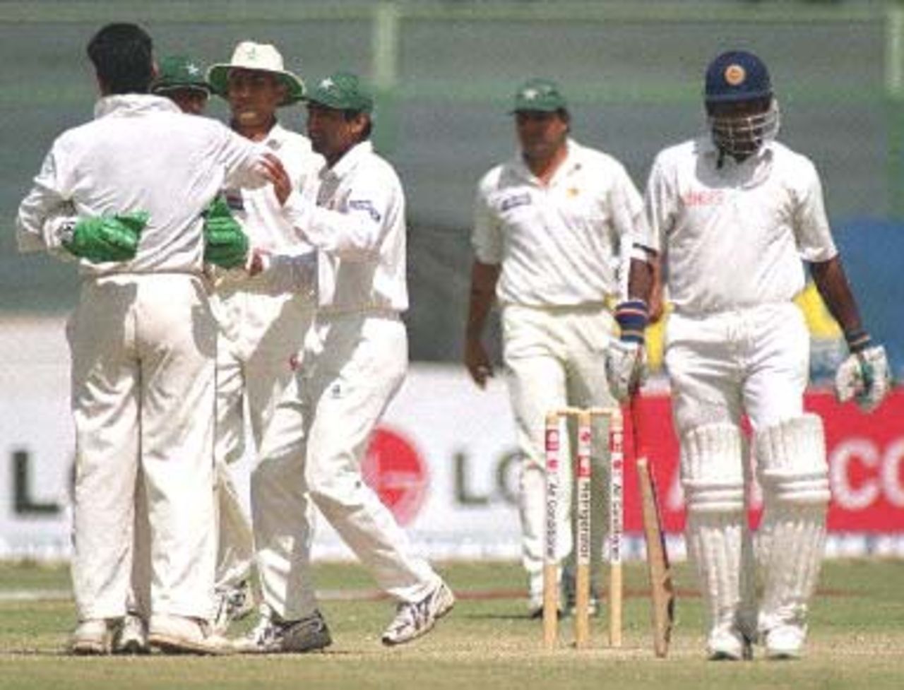 Members of the Pakistani team embrace their pacer Waqar Younis (L) as Sri Lankan skipper Sanath Jayasuriya (R) leaves the ground on the fourth day of the third and final cricket Test in Karachi, 15 March 2000. Jayasuriya was judged leg before wicket off Younis for 10. Sri Lanka were struggling at 127-6 at tea in reply of Pakistan's 450 runs lead.