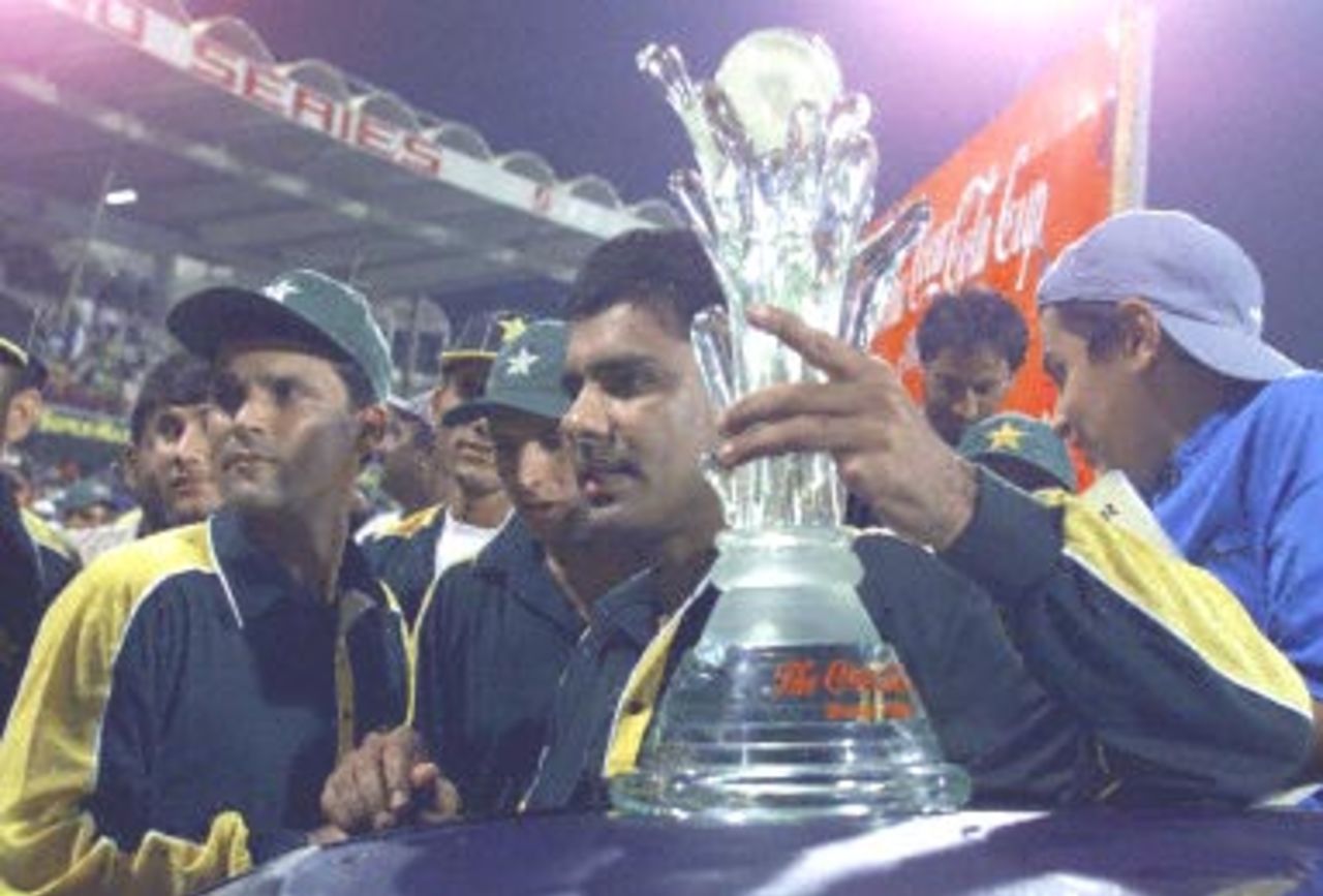 Pakistan cricket player Waqar Younis (C) holds the CC Trophy as the team captain Moin Khan (L) looks on after defeating South Africa by 16 runs in Sharjah 31 March 2000.