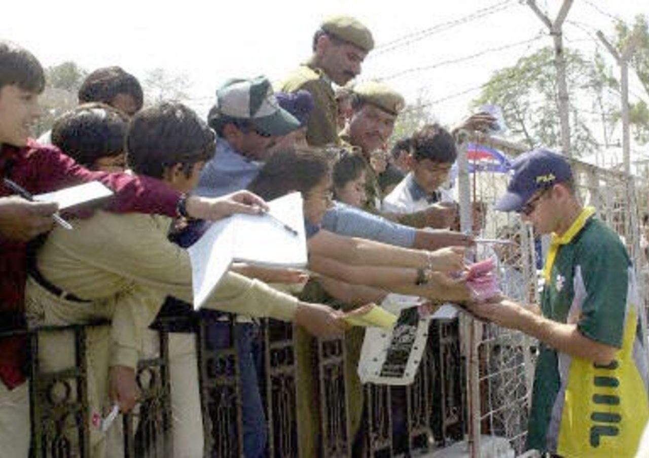 Children and policemen reach out for autographs from Australian batsman Adam Gilchrist (R) during a three-day cricket match against Board of Presidents in New Delhi 06 March 2001. Australia scored 413 for eight wicket in their first innings.