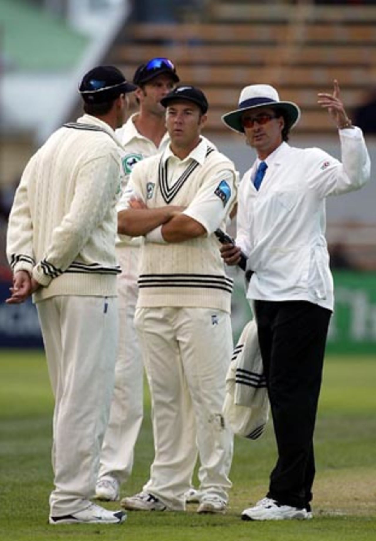 New Zealand players Stephen Fleming (captain, left), Chris Cairns (obscured) and Craig McMillan discuss the situation with umpire Brent Bowden as play is called to a halt due to bad light. 1st Test: New Zealand v England at Jade Stadium, Christchurch, 13-17 March 2002 (14 March 2002).