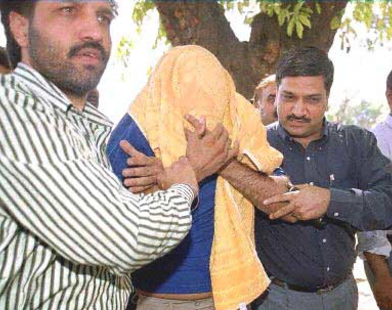 Indian businessman Rakesh Kalra (C-face covered in a cloth), implicated in a match-fixing scandal involving several South African cricket players, is produced to an Indian court by plainclothes policemen 09 April 2000 in New Delhi. Indian policemen have registered charges of criminal conspiracy against Indian Sanjiv Chawla, a London-based expatriate and four South African cricketers, including captain Hansie Cronjie, in the scandal which has rocked the cricketing world.