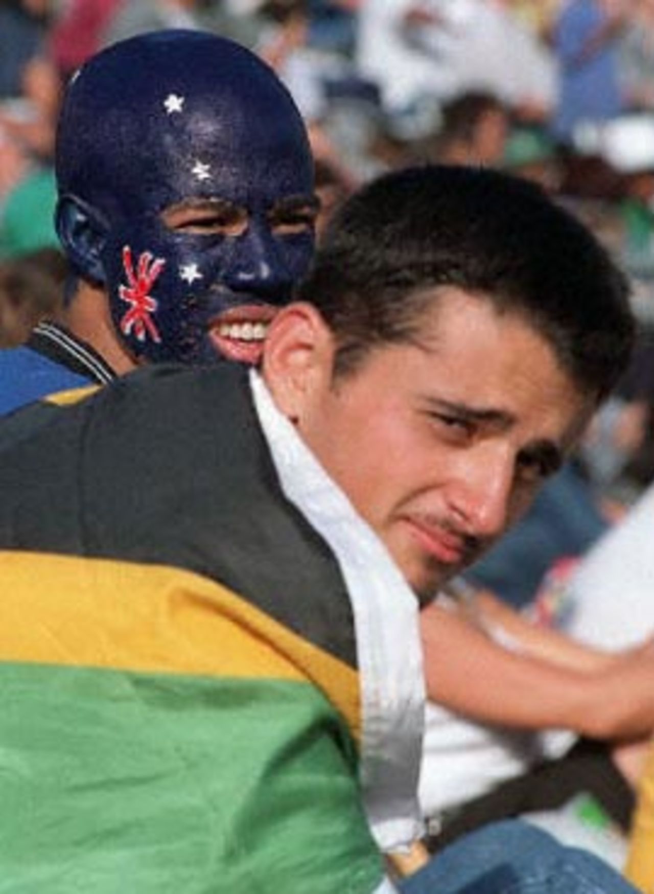 An Australian fan (L) who has his face painted with the Australian flag stands besides a local supporter who draped a South African flag over his body during the limited overs international played at Newlands in Cape Town 14 April 2000. The Australia vs South Africa's match is the second of three one day internationals being played in South Africa