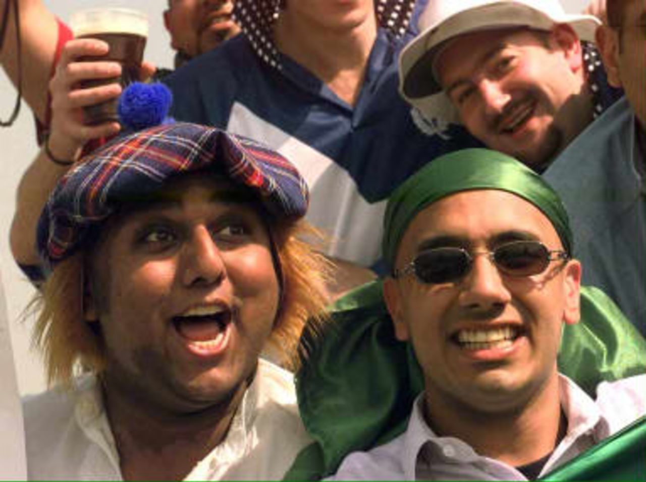 Pakistan cricket supporters enter into the spirit of the 'Carnival of Cricket' as one wears a Scottish hat and wig while the other wears more traditional Pakistani colours during their Cricket World Cup Match against Scotland at Chester-le-Street 20 May, 1999.