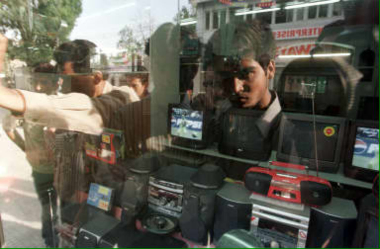 Local residents are reflected in the window of an electronics shop, as they watch the cricket WC99 match, India against Pakistan on television 08 June 1999 in Srinagar. Most Kashmiris are rooting for Pakistan, currently involved in cross-border shelling with India