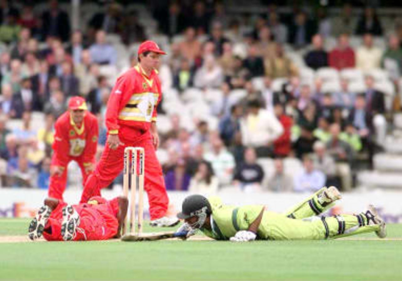 Pakistan opening batsman, Saeed Anwar (Right) dives to the crease just in time to escape a runout by Henry Olonga (Left grounded) who missed the stumps with his throw during their World Cup match against Zimbabwe at the Oval in London, 11 June 1999.