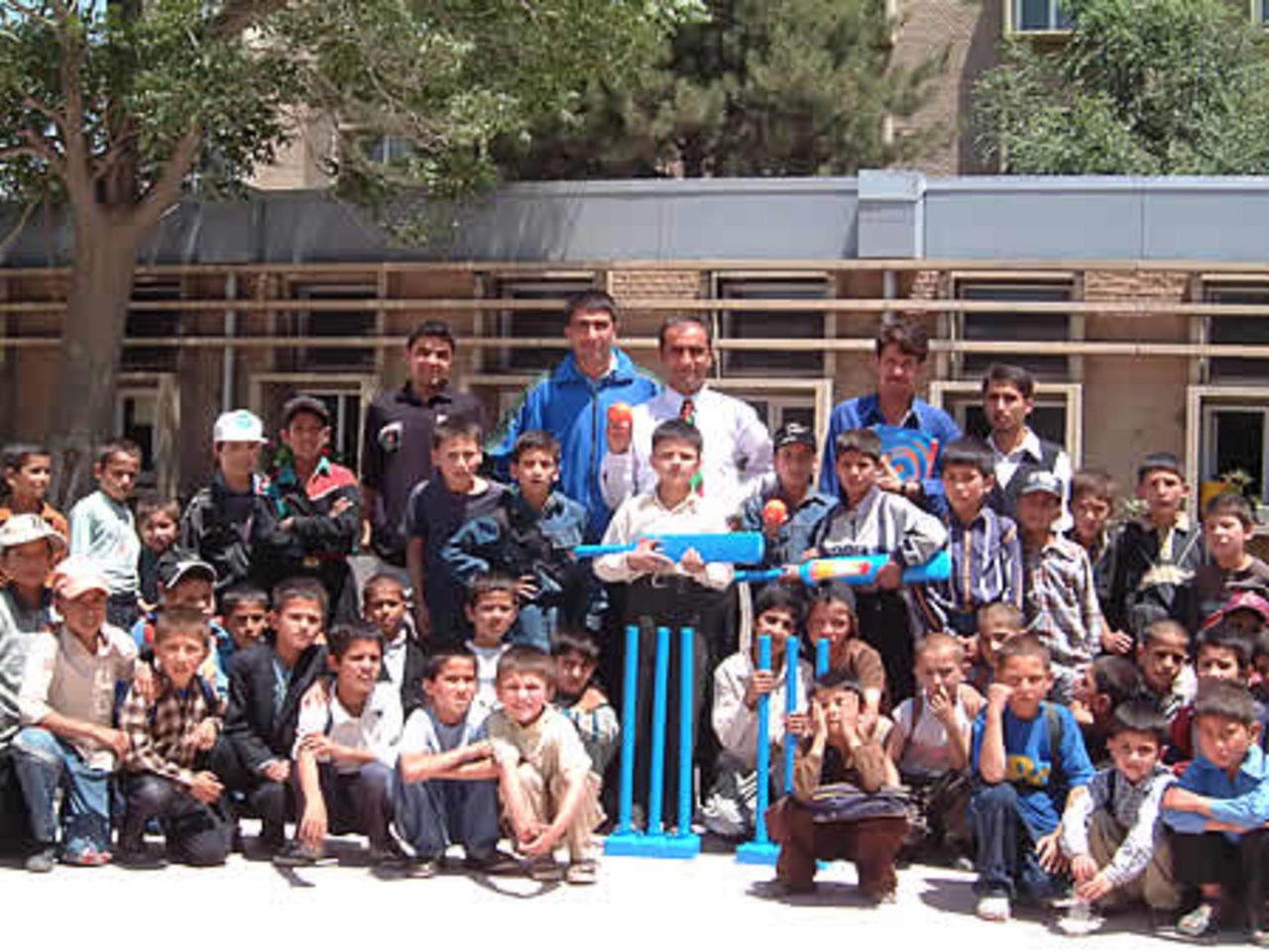 Taj Malik, Afghan National coach (white shirt and tie) with Abdul Khalil GM ACF and Khaliq Dad Noori Director Kabul Cricket Association along with students and staff of Amani High School receiving Kwik cricket set donated by ECB.