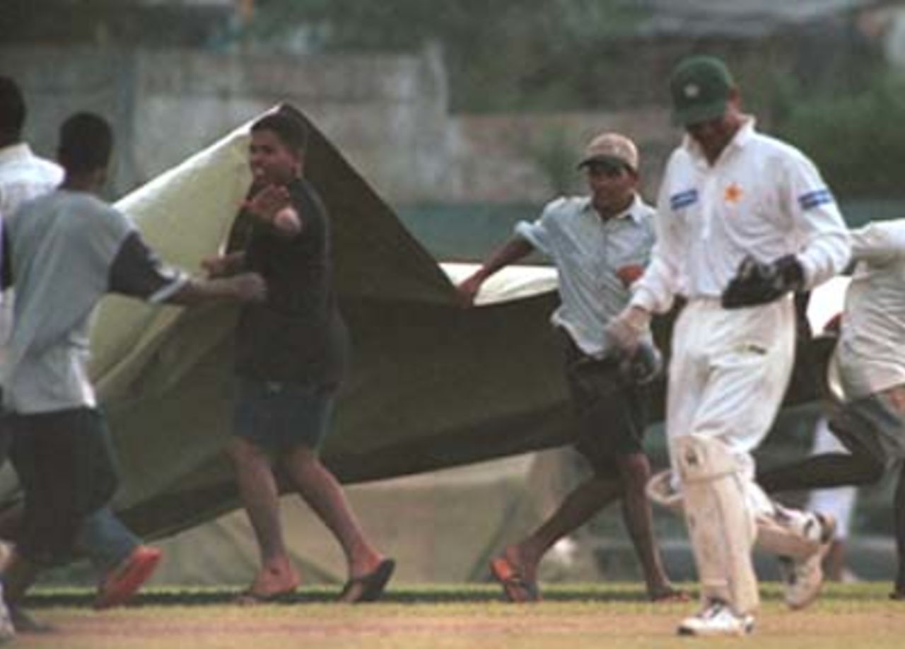 Ground staff collect water from covers as Moin Khan walks out during the third day of the third cricket Test between Sri Lanka and Pakistan in Asgiriya International cricket stadium in Kandy, Sri Lanka on Friday, June. 30, 2000