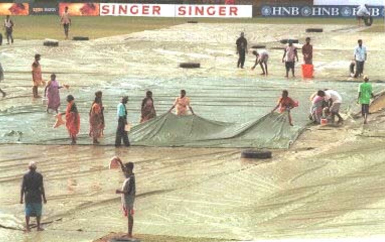 Ground staff collect water from covers during the fourth day of the third and final cricket Test between Sri Lanka and Pakistan in Asgiriya International cricket stadium in Kandy 01 July, 2000. No play was possible during the day due to continuous rain and wet ground conditions.