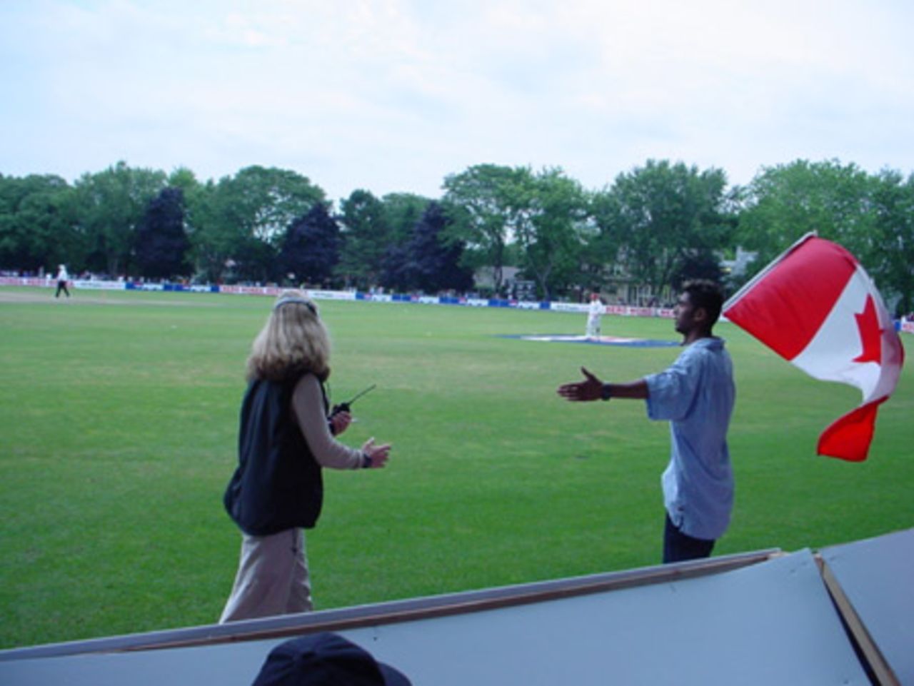 A happy flag-bearing Canadian fan wanders around the boundary after the end of the Scotland innings as a television crew member tries to keep him outside the rope. ICC Trophy 2001: Canada v Scotland at Toronto, Cricket, Skating and Curling Club, 17 July 2001.