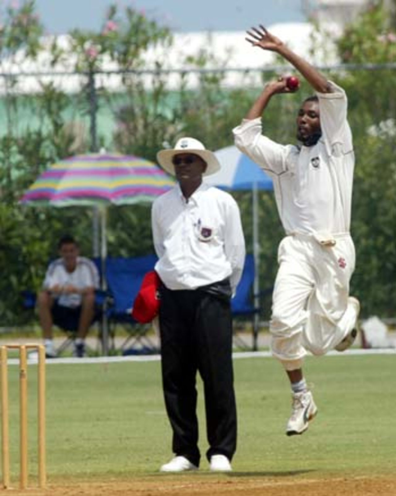 Austin Codrington (Canada) in delivery stride. Umpire is Steve Kalloo (USA).