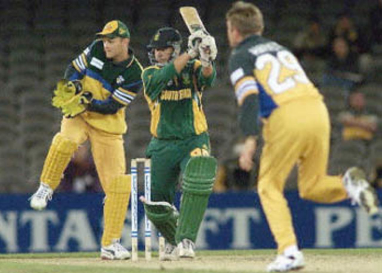 Bowler Ian Harvey and wicketkeeper Adam Gilchrist look on as Andrew Hall smashes the ball to the boundary in their one day cricket match being played under a closed roof at the Colonial Stadium in Melbourne. Being played in the middle of winter in Melbourne, South Africa is 129-4 in the 33rd over but Australia leads the three match series 1-0. South Africa in Australia, 2000/01, 2nd One-Day International, Australia v South Africa, Colonial Stadium, Melbourne, 18 August 2000.