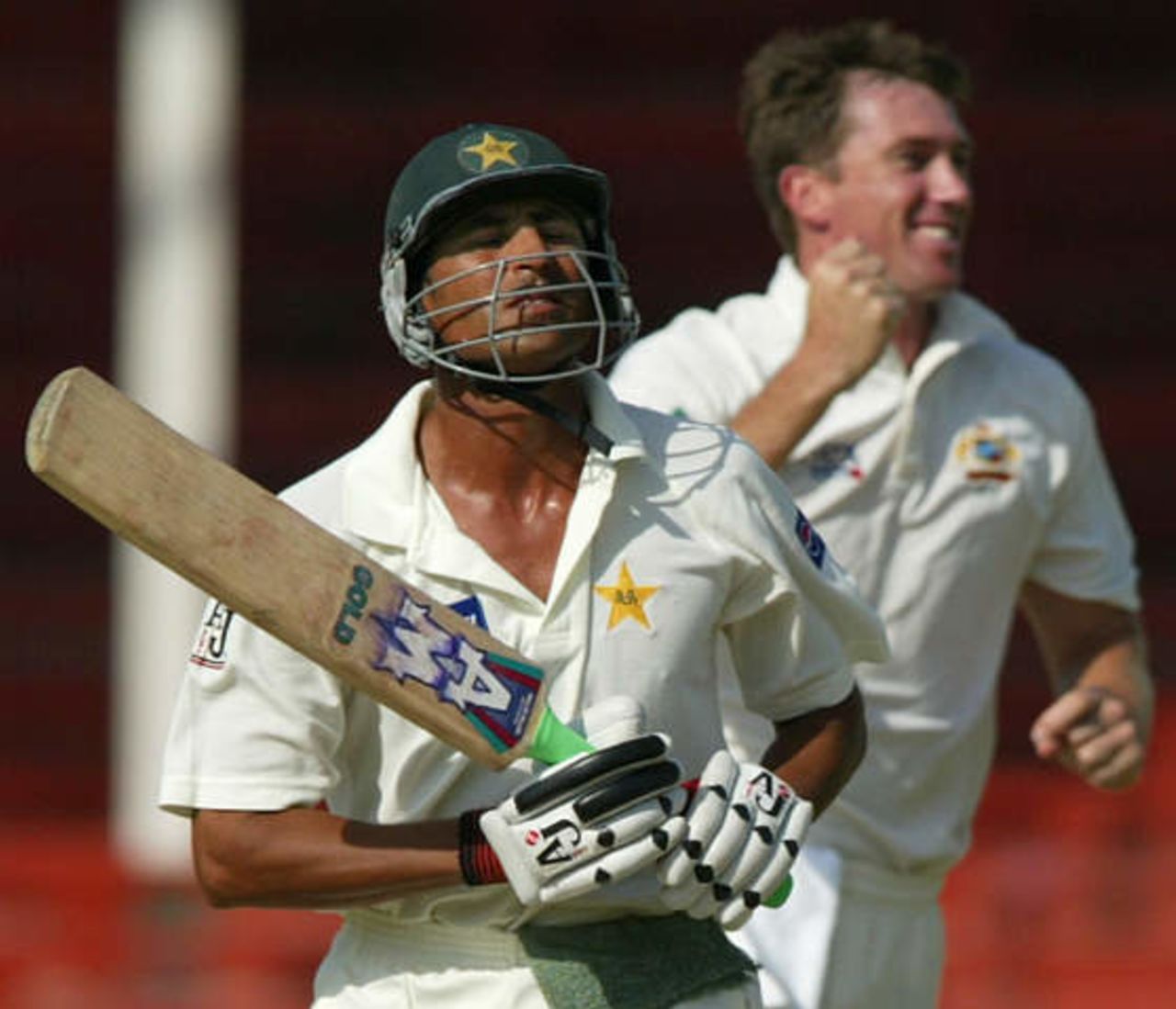 Pakistan's vice captain Younis Khan (L) grimaces after his dismissal by LBW as Australian fast bowler Glenn McGrath celebrates at Sharjah's stadium October 12, 2002 on the second day of their second cricket test match. The second and third tests are being held in the neutral venue of Sharjah after Australia balked at playing in Pakistan due to security concerns.