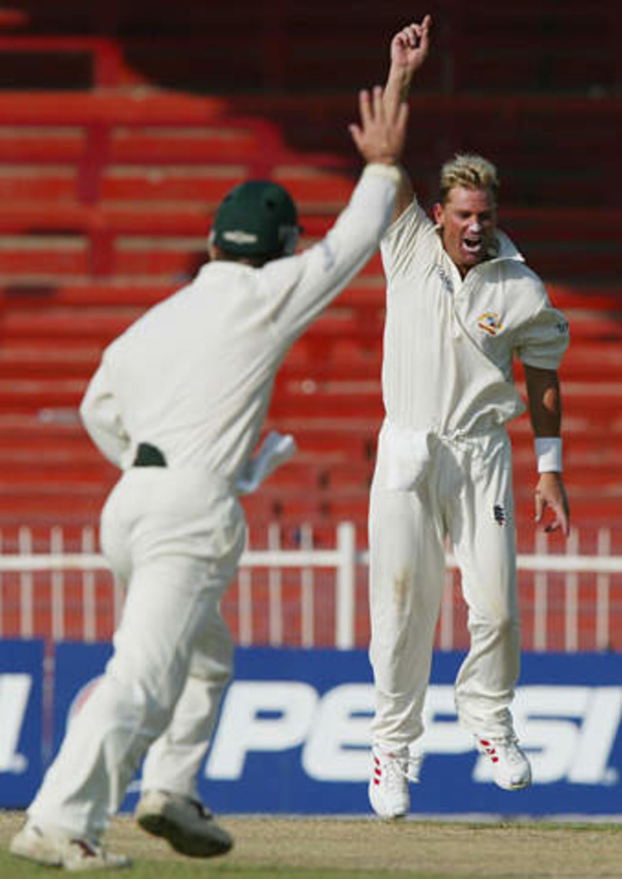 Australian spin bowler Shane Warne and team mate Justin Langer (L) celebrate the dismissal of Pakistan's Imran Nazir at Sharjah's stadium October 12, 2002 on the second day of their second cricket test match. The second and third tests are being held in the neutral venue of Sharjah after Australia balked at playing in Pakistan due to security concerns.