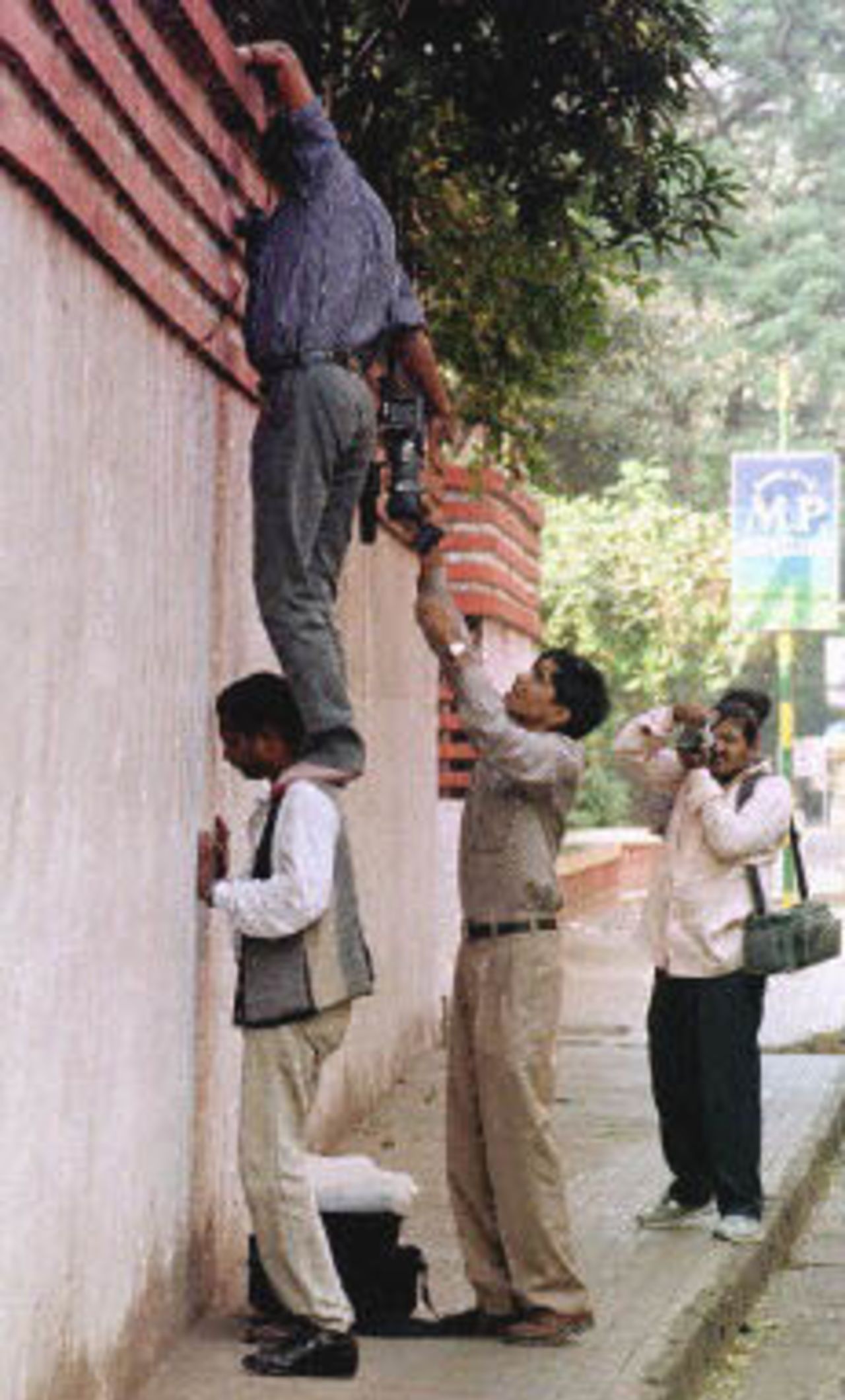 Indian cameramen scale a wall as they try to get some inside shots of the residence of former International Cricket Council (ICC) President Jagamohan Dalmiya in Calcutta, 13 November 2000 after Central Bureau of Investigation (CBI) officers raided his house. The CBI search was in connection with a probe into alleged irregularities in the granting of TV rights to telecast cricket matches.