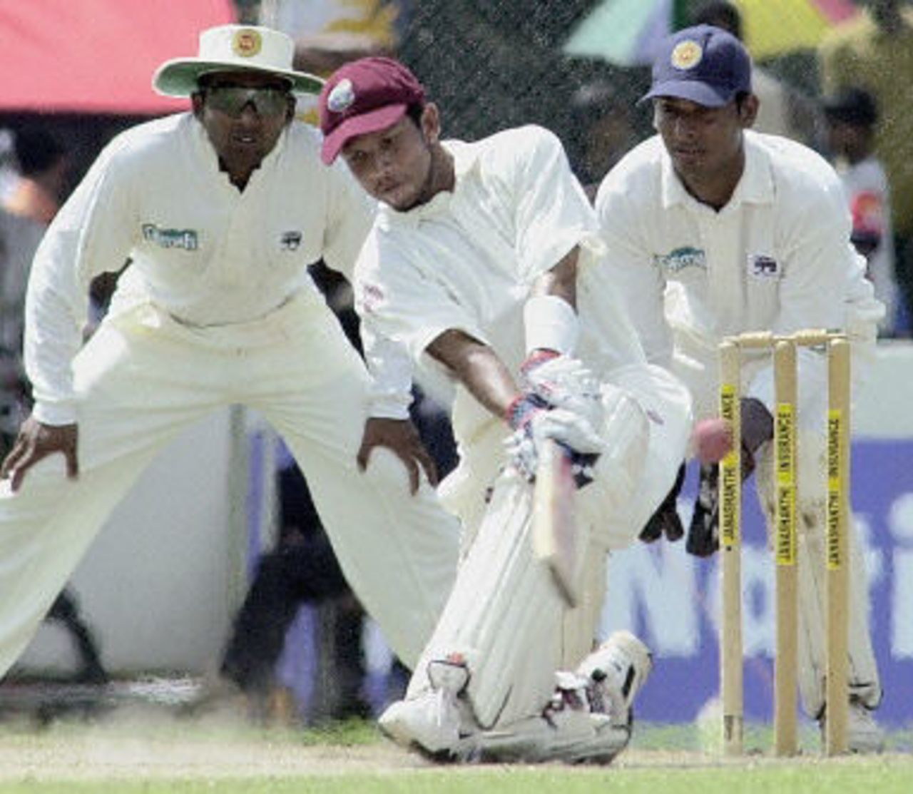 Ramnaresh Sarwan sweeps a ball as fielder Mahela Jayawardena  and wicketkeeper Kumar Sangakkara looks on