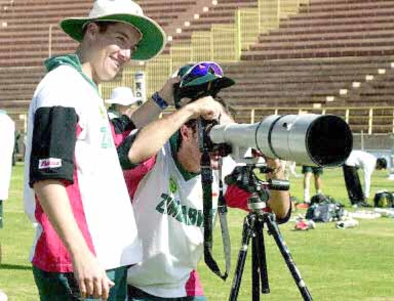 Zimbabwe cricketer Dirk Viljoen looks through a photographer's camera as his teammate Travis Friend (L) holds his cap during a practice session at Jodhpur cricket ground 07 December 2000, in Jodhpur. Zimbabwe will play its third one-day cricket match against India 08 December. India leads the series 2-0.