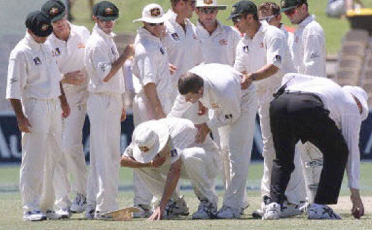 Australian players look on with concern to bowler Jason Gillespie (bottom-C) after he was hit in the face by the ball, being picked up by umpire Steve Davis (R), after the players ran in to congratulate Stuart MacGill (C-behind Gillespie) on taking a wicket on day four of the third Test match at the Adelaide Oval, 18 December 2000. Australia now only need to score 32 runs 19 December to win the match with six wickets in hand.