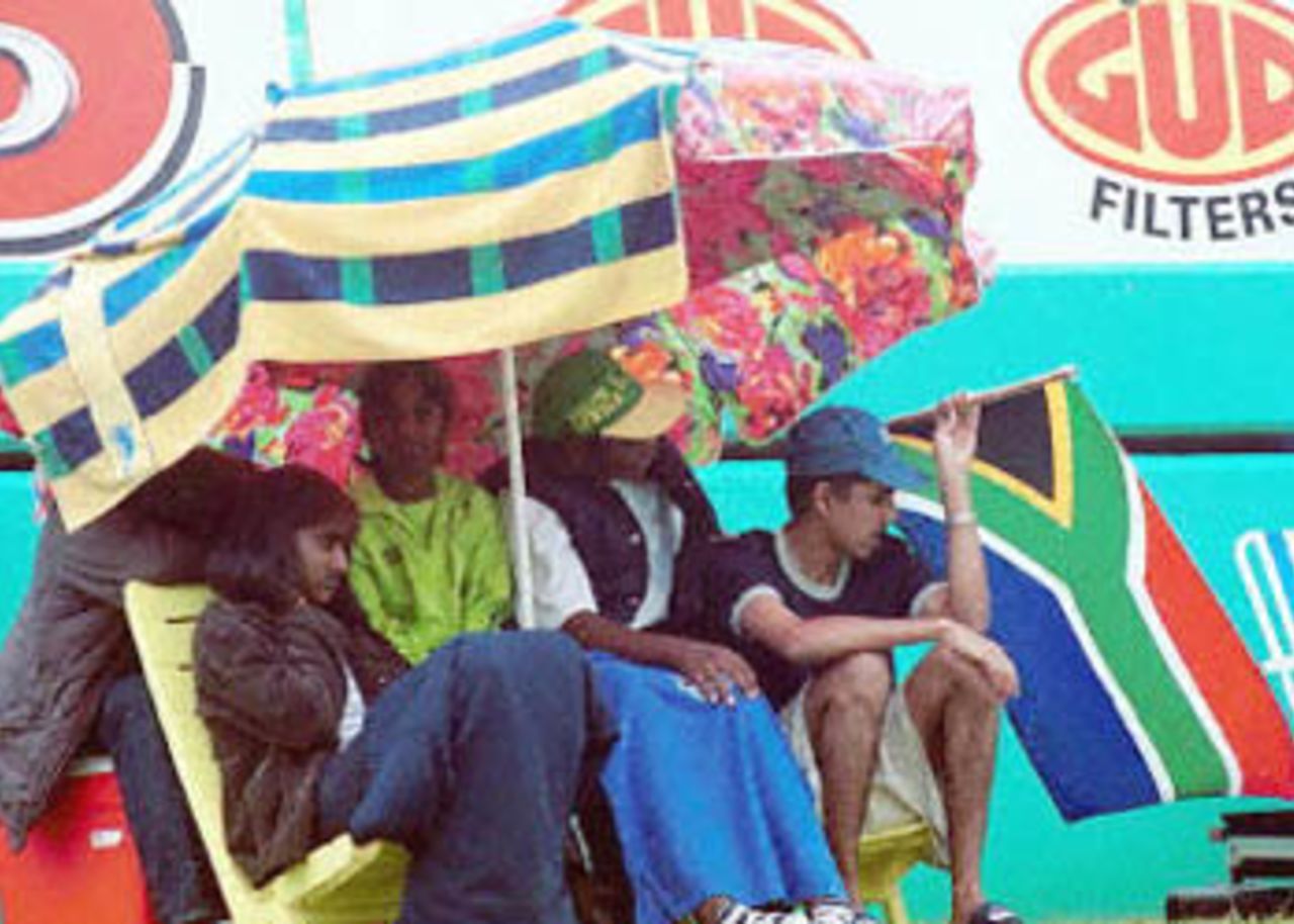 Disappointed South African supporters tuck themselves under cover as rain continues to disrupt the fourth day of the first cricket Test match between South Africa and Sri Lanka 29 December 2000 at Durban's Kingsmead cricket grounds. Play was called off without a ball being bowled due to rain.