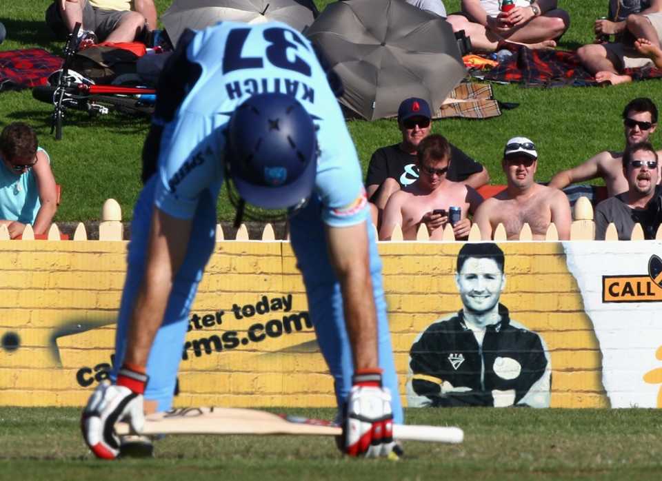 Simon Katich stretches in front of an advertising sign featuring Michael Clarke