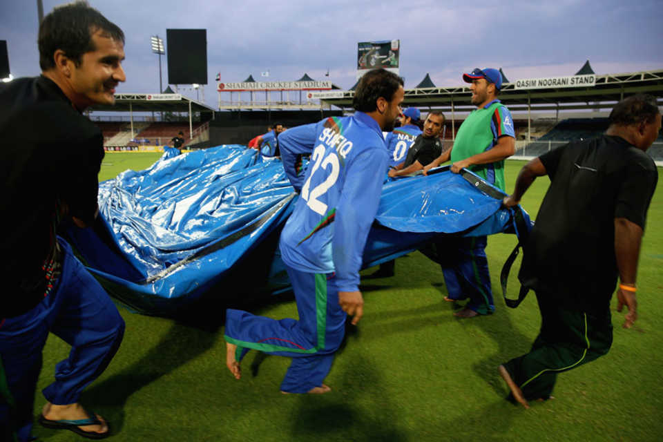 Afghanistan players help clear the covers off the ground